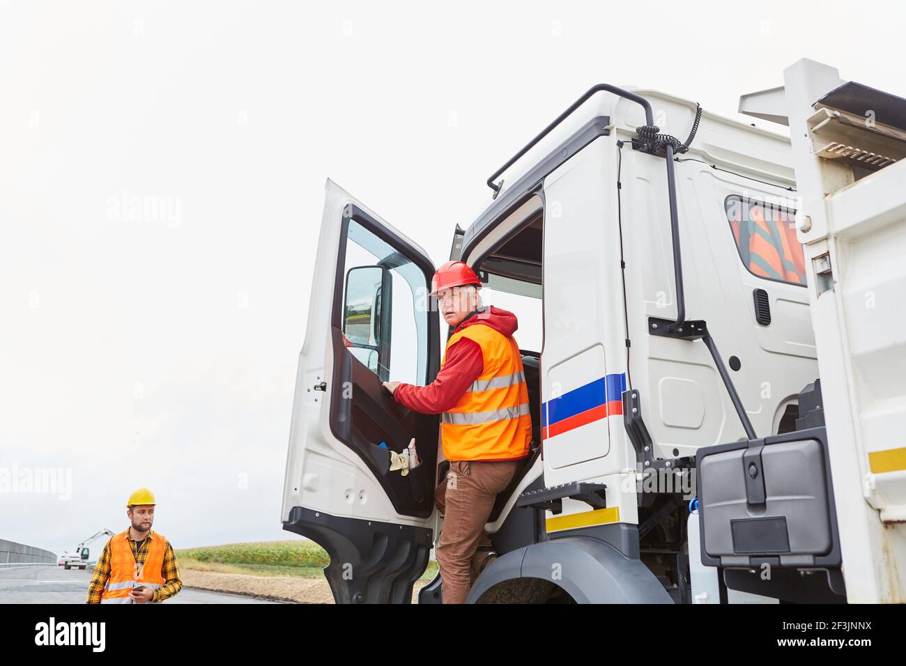 Fahrer in der LKW-Kabine auf der Baustelle von Straßenbau bringt Lieferung von Baumaterial Stockfoto