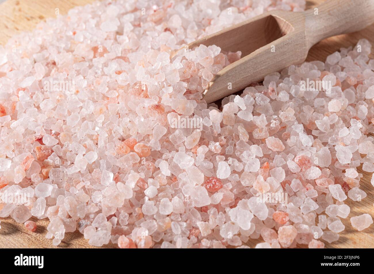 Rosa himalaya-Salz. Nahaufnahme Himalayan Pink Rock Salt in Holzlöffel auf schwarzem Hintergrund. Draufsicht. Haufen grobkörniges Salz Stockfoto