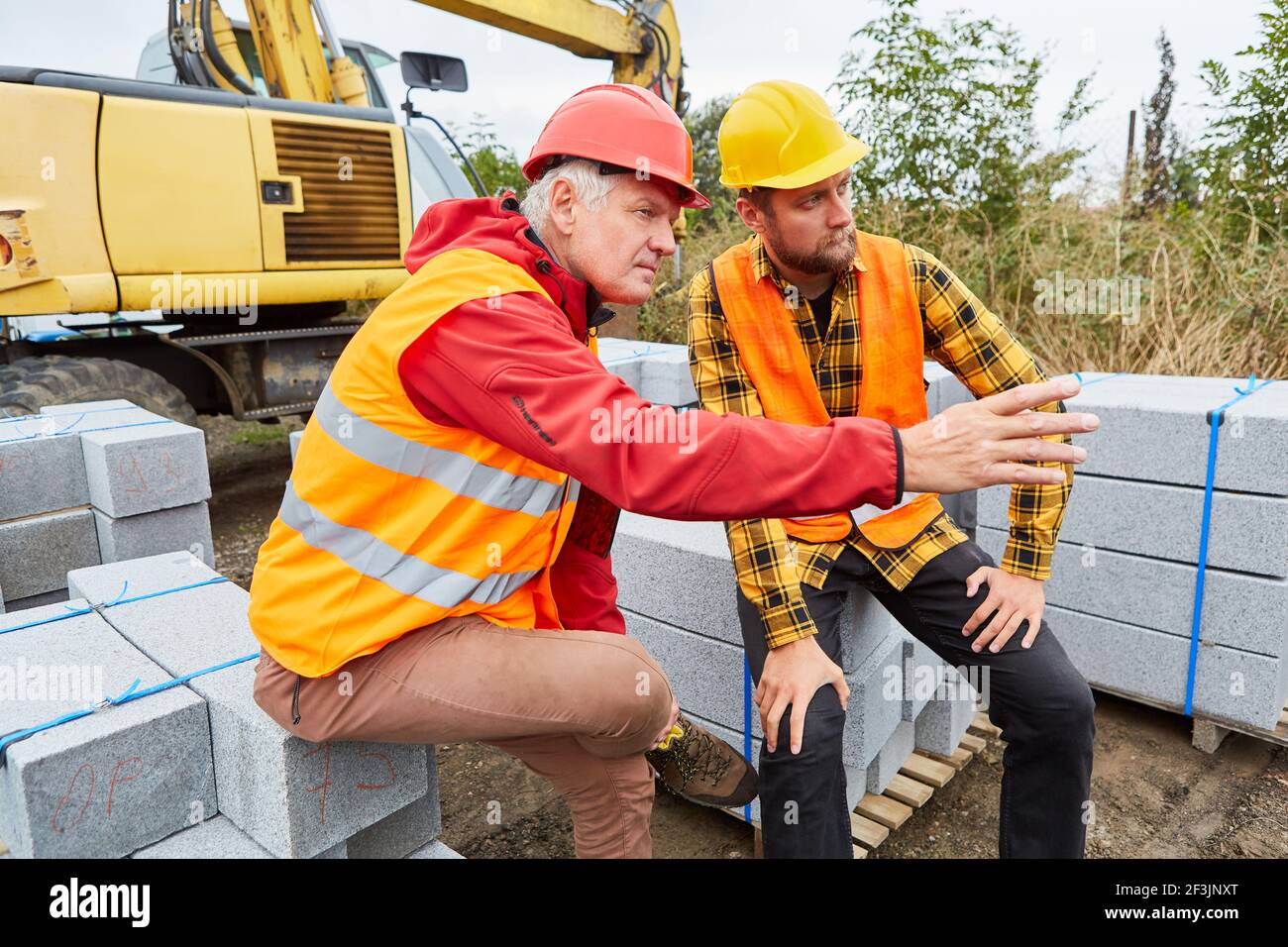 Zwei Bauarbeiter auf der Baustelle des Hausbaus Mit Baustoffen und Bagger Stockfoto