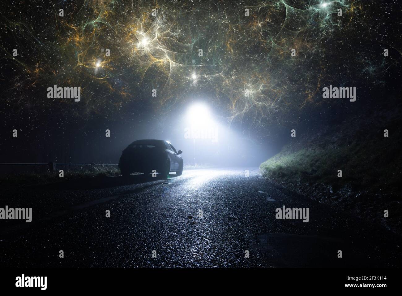 Ein einbahniges Auto, geparkt auf der Seite der Straße, unter einer Ampel, auf einer gruseligen Landstraße. In einer nebligen Winternacht. Mit apokalyptischen Wolken Stockfoto
