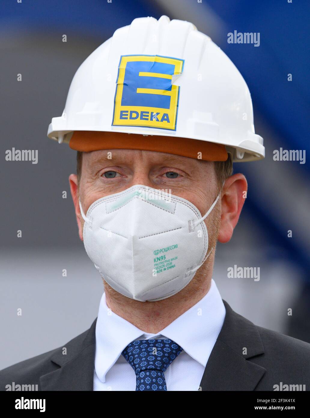 Berbersdorf, Deutschland. März 2021, 12th. Der sächsische Ministerpräsident Michael Kretschmer (CDU) nimmt am symbolischen Spatenstich für den Ausbau des Logistikzentrums Edeka in Berbersdorf Teil und trägt einen Bauhelm mit dem Edeka-Logo. Der Ausbau des bestehenden Logistikzentrums und der Umbau der kürzlich erworbenen Logistikhalle Landgard werden knapp 93 Millionen Euro kosten. Sie ist damit eine der umfangreichsten Investitionen, die im ersten Halbjahr trotz Corona in Sachsen beginnen. Quelle: Robert Michael/dpa-Zentralbild/dpa/Alamy Live News Stockfoto