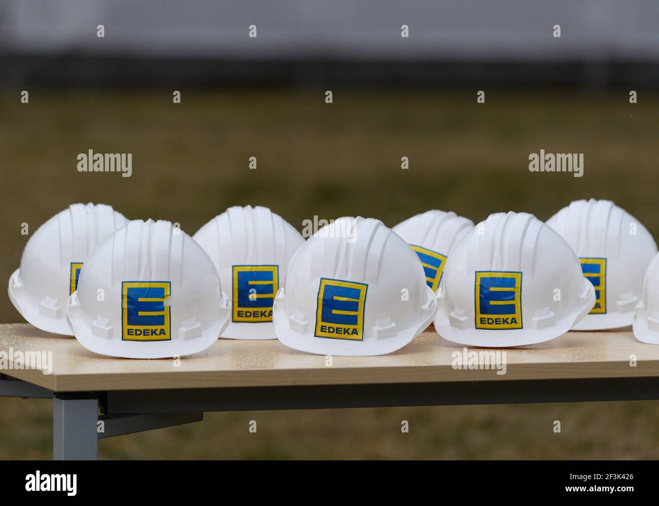 Berbersdorf, Deutschland. März 2021, 12th. Bauhelme mit dem Edeka-Logo liegen vor dem symbolischen Spatenstich für den Ausbau des Edeka-Logistikzentrums in Berbersdorf auf einem Tisch. Der Ausbau des bestehenden Logistikzentrums und der Umbau der kürzlich erworbenen Logistikhalle von Landgard werden knapp 93 Millionen Euro kosten. Sie ist damit eine der umfangreichsten Investitionen, die im ersten Halbjahr trotz Corona in Sachsen beginnen. Quelle: Robert Michael/dpa-Zentralbild/dpa/Alamy Live News Stockfoto