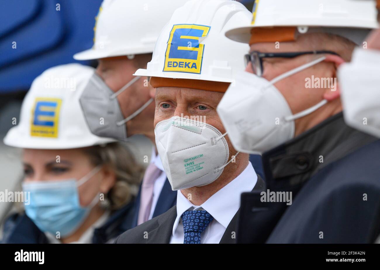 Berbersdorf, Deutschland. März 2021, 12th. Der sächsische Ministerpräsident Michael Kretschmer (CDU, M.) nimmt am symbolischen Spatenstich für den Ausbau des Logistikzentrums Edeka in Berbersdorf Teil und trägt einen Bauhelm mit dem Edeka-Logo. Der Ausbau des bestehenden Logistikzentrums und der Umbau der kürzlich erworbenen Logistikhalle Landgard werden knapp 93 Millionen Euro kosten. Sie ist damit eine der umfangreichsten Investitionen, die im ersten Halbjahr trotz Corona in Sachsen beginnen. Quelle: Robert Michael/dpa-Zentralbild/dpa/Alamy Live News Stockfoto