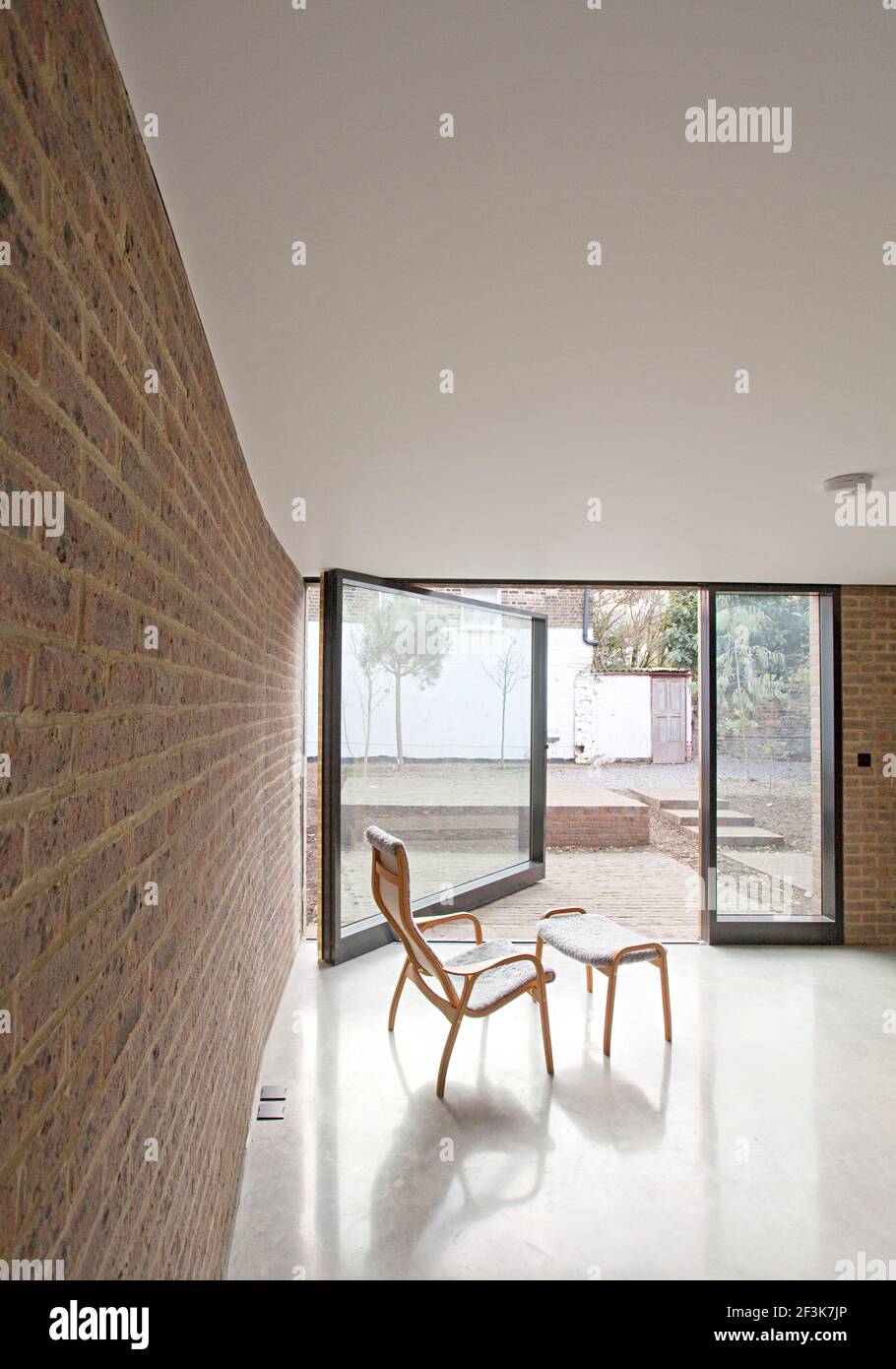 Duggan Morris Haus: Kings Grove, Peckham, London. Das Foto zeigt den Hauptwohnbereich mit gebogenem Holzstuhl und dem schwenkbaren Fenster Stockfoto
