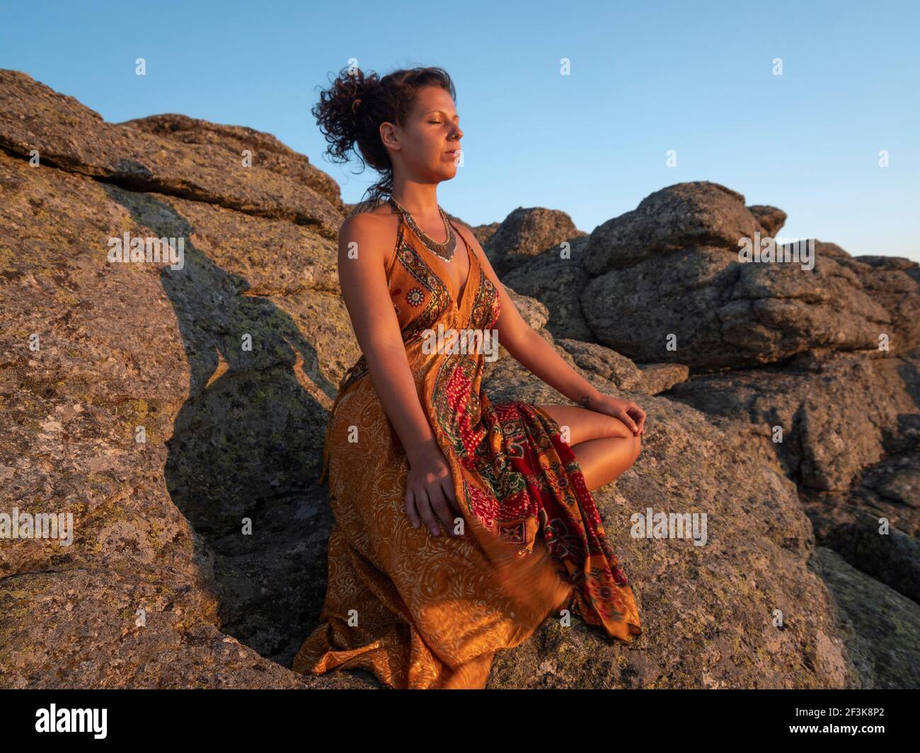 Kaukasische Frau mit seidenorangefarbenem Kleid, die im Sonnenuntergang meditiert. Stockfoto