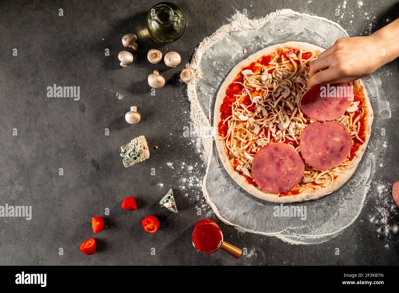 Eine Pizza zubereiten, den Schinken auf den Teig legen Stockfoto
