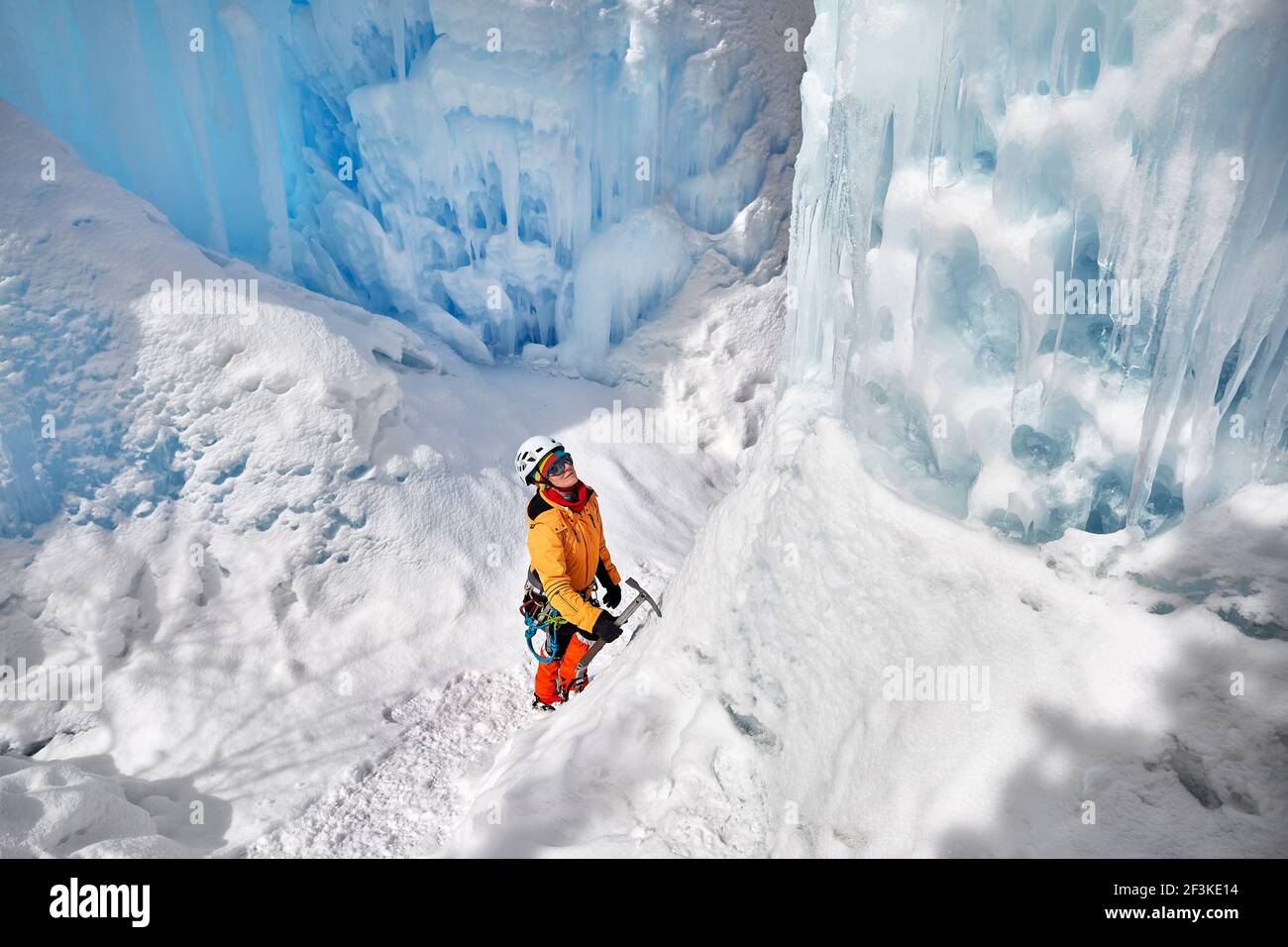 Frau Kletterin in oranger Jacke mit Eispickel in der Nähe von gefrorenen Wasserfall in den Bergen in Almaty, Kasachstan Stockfoto