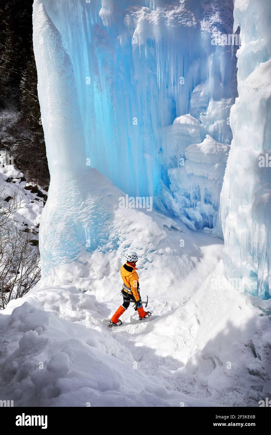 Frau Kletterin in oranger Jacke mit Eispickel beim Spaziergang in der Nähe von gefrorenen Wasserfall in den Bergen in Almaty, Kasachstan Stockfoto