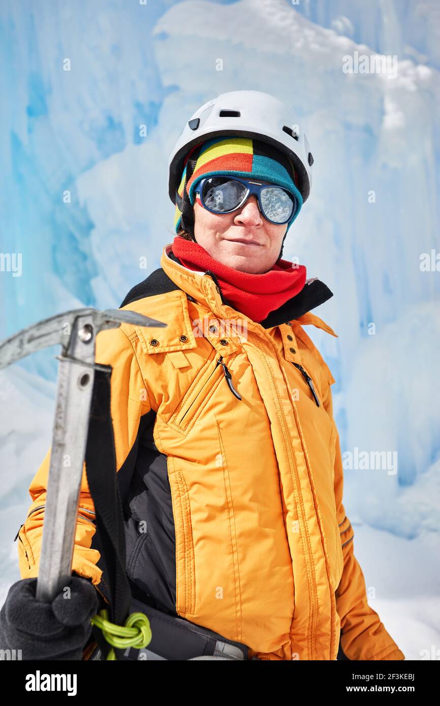 Portrait einer Bergsteigerin in oranger Jacke mit Eispickel in der Nähe eines gefrorenen Wasserfalls in den Bergen in Almaty, Kasachstan Stockfoto