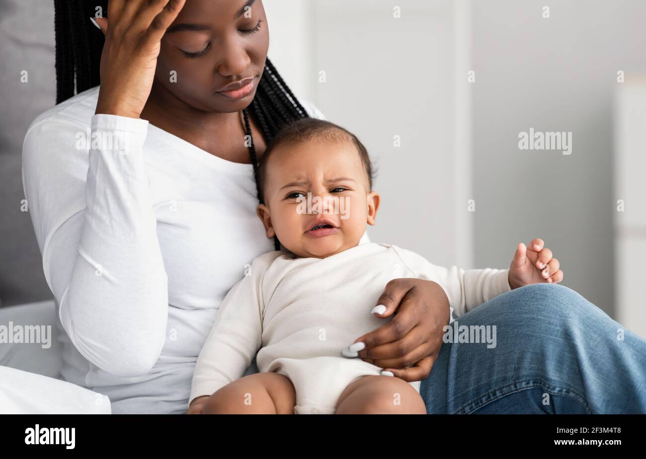 Gestresste afroamerikanische Mutter sitzt mit Kind auf dem Bett Stockfoto