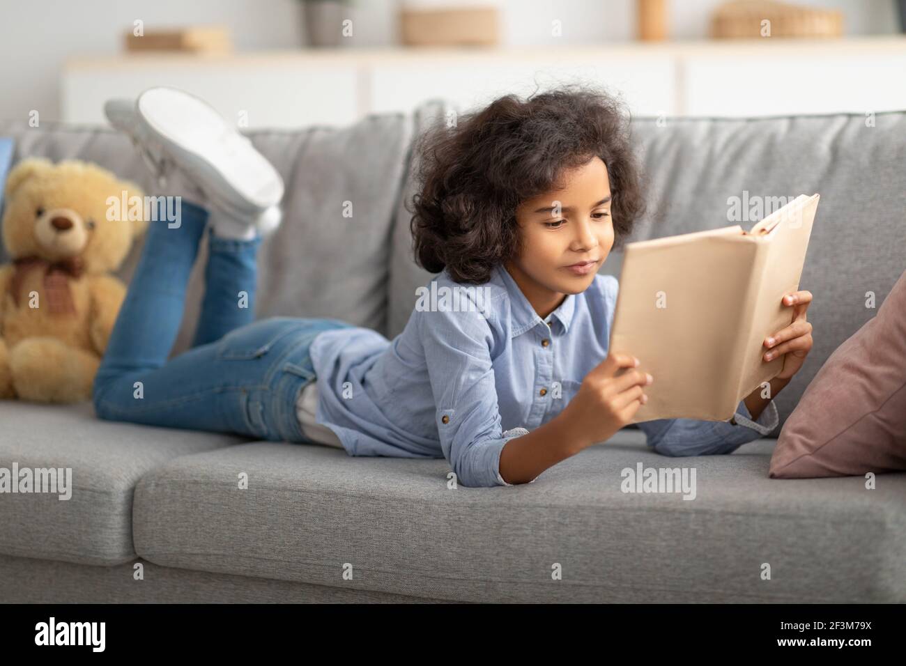 Schwarzes Mädchen auf dem Sofa liegend, Buch lesend Stockfoto