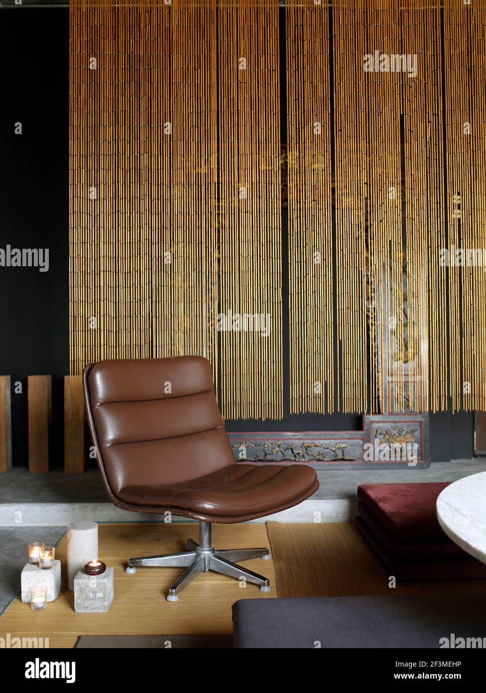 Drehstuhl aus braunem Leder vor Bambusvorhang in moderner Wohnung, Singapur Stockfoto