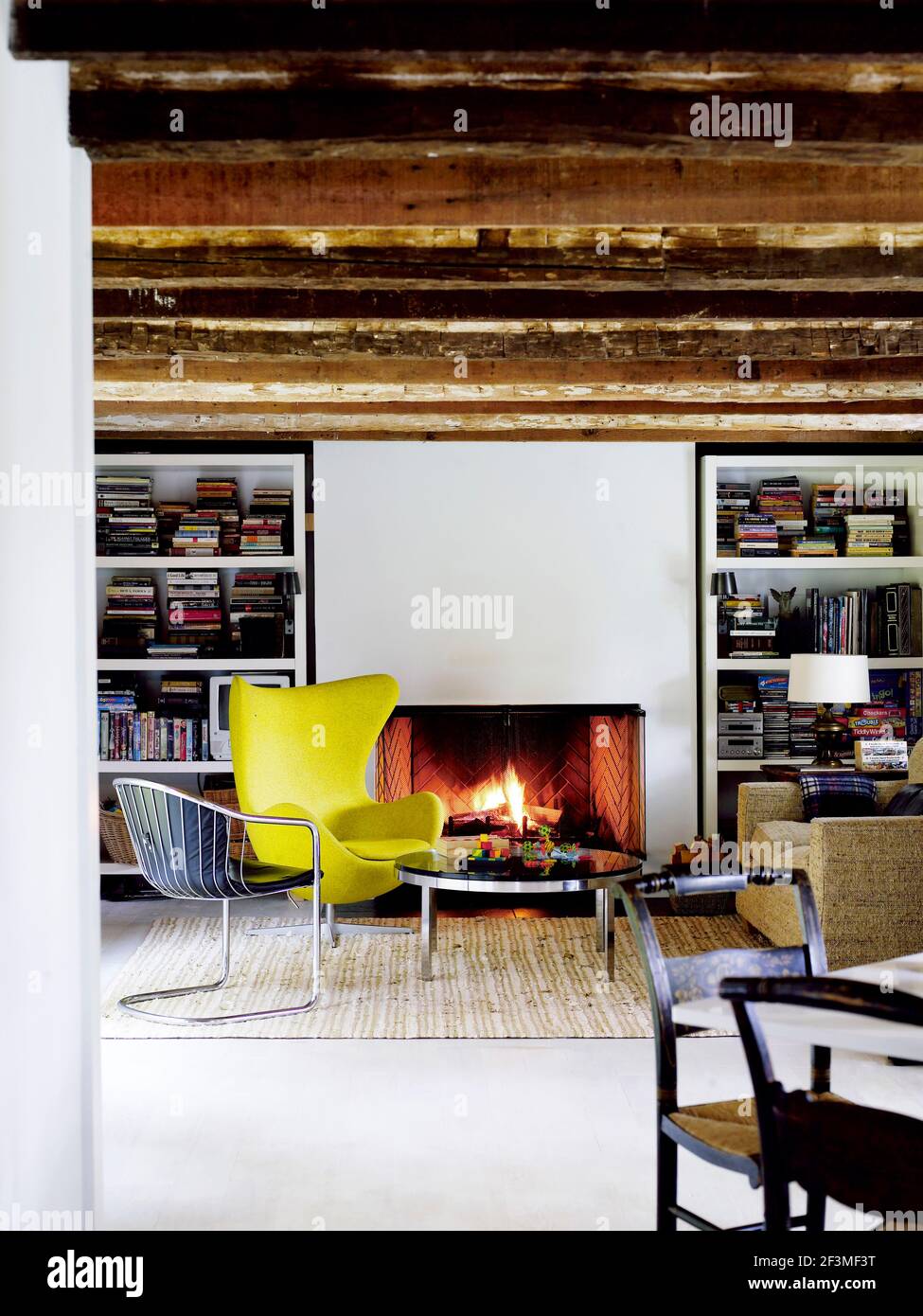 Stühle und runder Couchtisch vor offenem Feuer, flankiert von Regalen im Zimmer mit Balkendecke in Larson, New York, USA Stockfoto