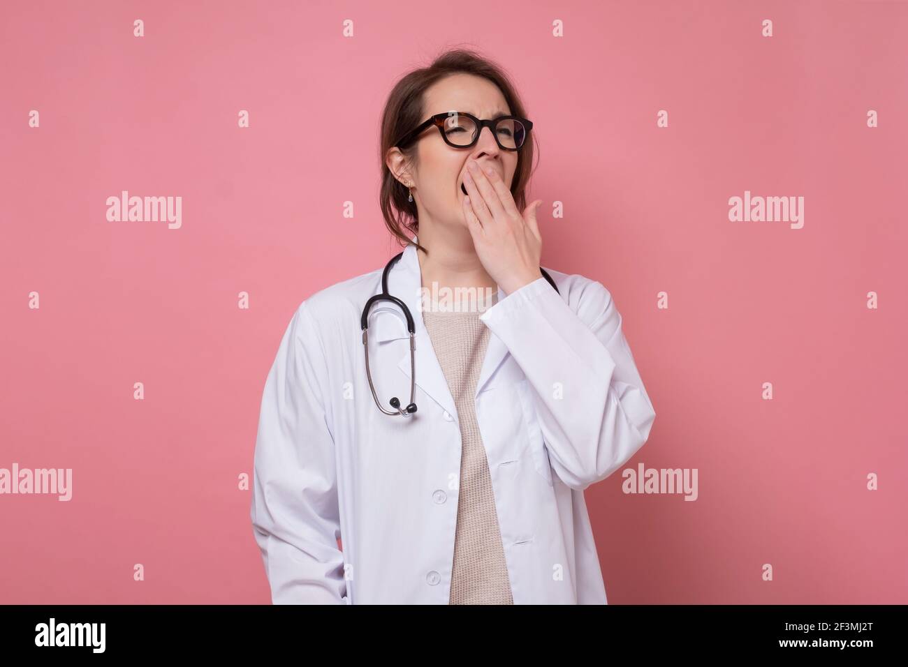 Junge schöne müde Arzt Frau trägt Stethoskop und Brille auf blauem Hintergrund gähnende Frau über den Mund mit der Hand. Unruhig und schläfrige Stockfoto