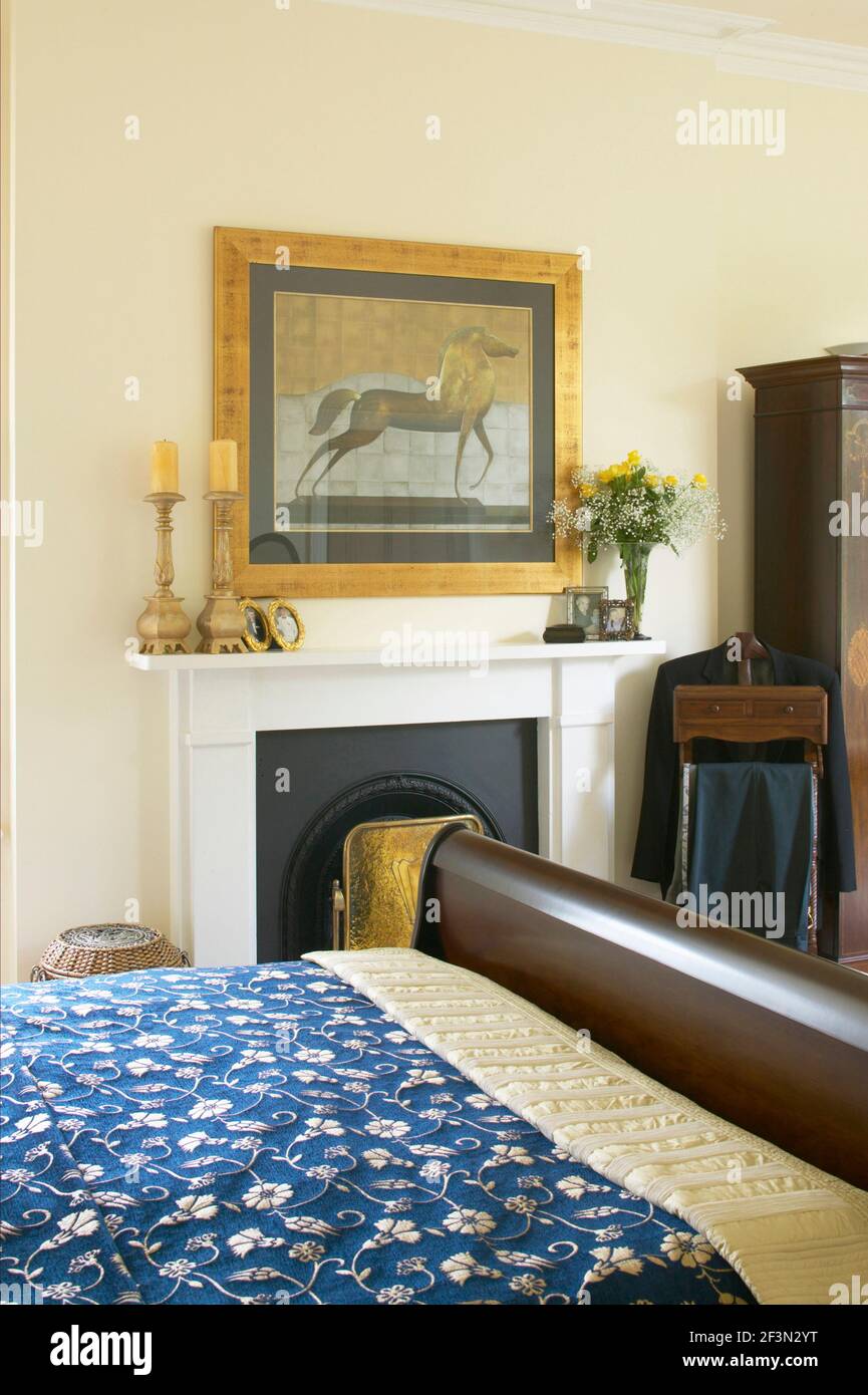 Traditionelle blassgelbe Schlafzimmer Detail mit Holzschlitten Bett und Kamin mit Kunstwerken. Stockfoto