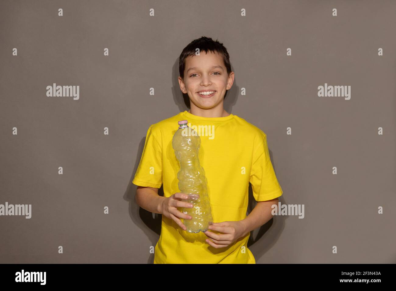 Junge Teenager Freiwillige hält Plastikflasche auf grauem Hintergrund im Studio und lächelt. Null Kunststoff, Recycling-Konzept. Speicherplatz kopieren Stockfoto