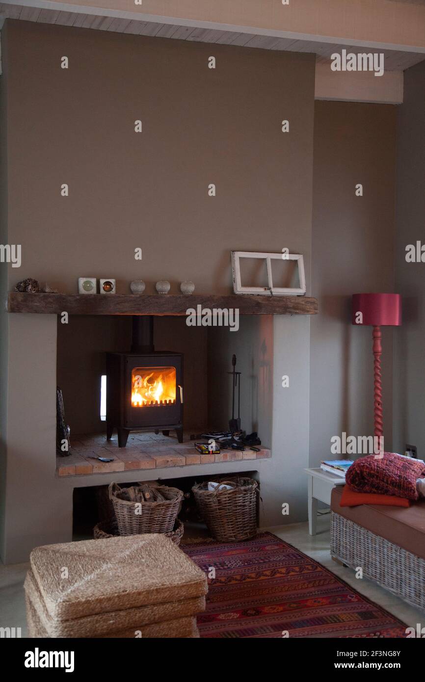 Entferntere Ansicht der Lounge mit Kamin, Rohrmöbeln mit neutralen Kissen und roten und verbrannten Orangen in der Dekoration Stockfoto