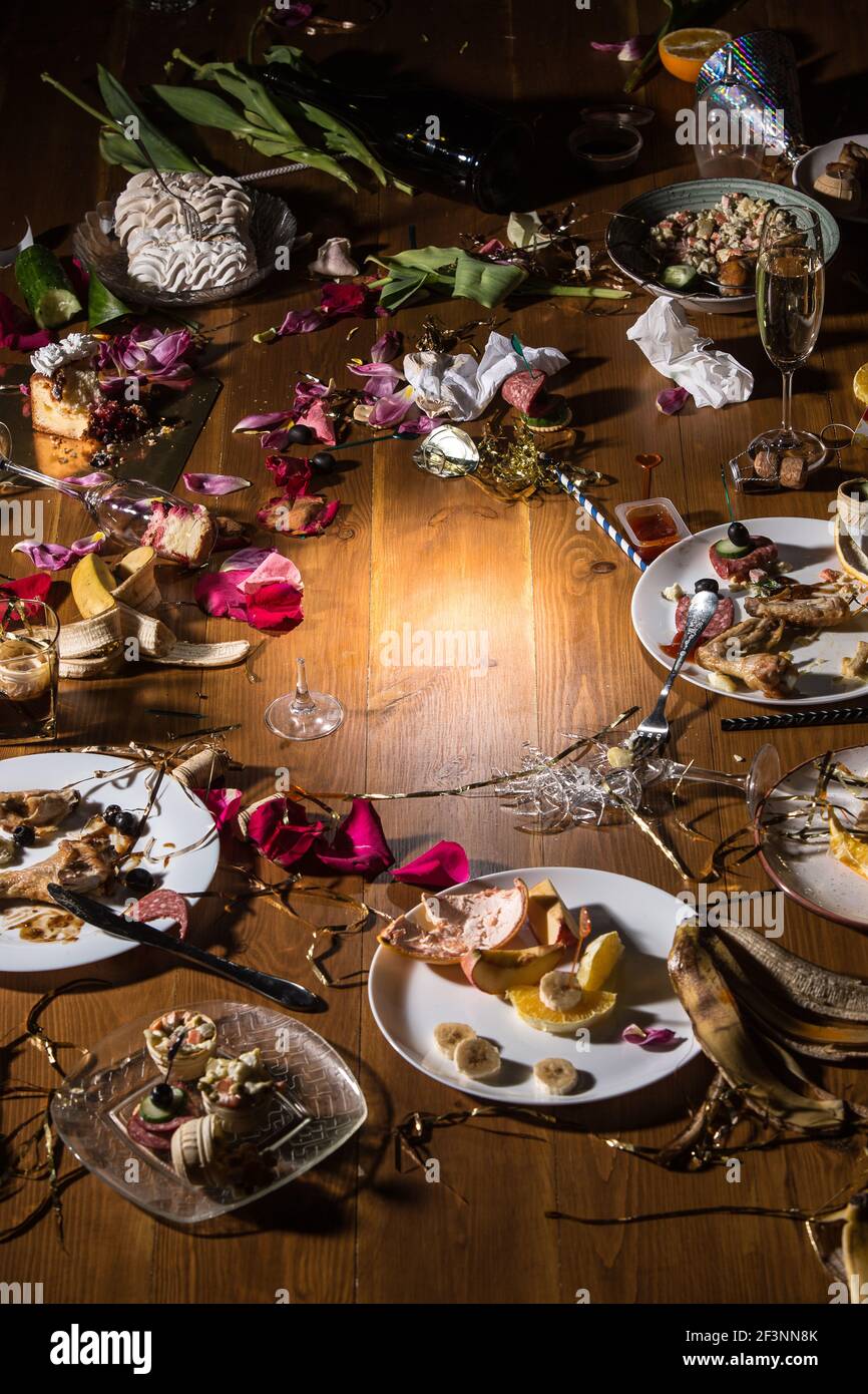 Am frühen Morgen nach der Party. Gläser und Teller auf dem Tisch mit Konfetti und Serpentin, Reste, Blütenblätter Stockfoto