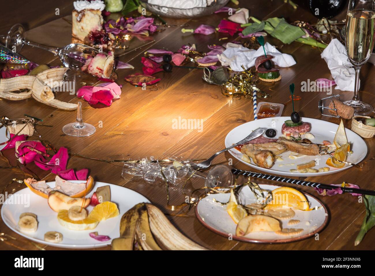 Am frühen Morgen nach der Party. Gläser und Teller auf dem Tisch mit Konfetti und Serpentin, Reste, Blütenblätter Stockfoto