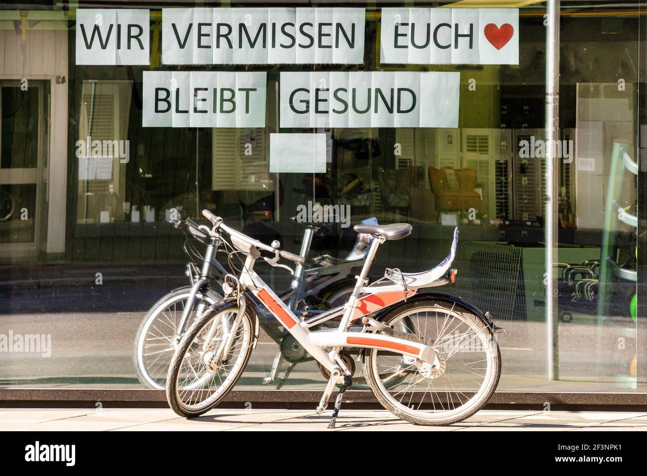 Schaufenster mit deutschem Hinweis : Wir vermissen euch. Bleibt gesund / Wir vermissen dich. Bleiben Sie gesund. Es gibt zwei Fahrräder vor dem Laden Stockfoto