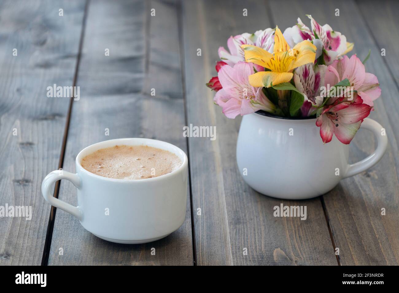 Weiße Tasse Kaffee mit bunten Alstroemerien in weißem Becher auf Holztisch. Rosa, gelbe und lila Blüten in Tasse. Konzept von Guten Morgen. Sof Stockfoto