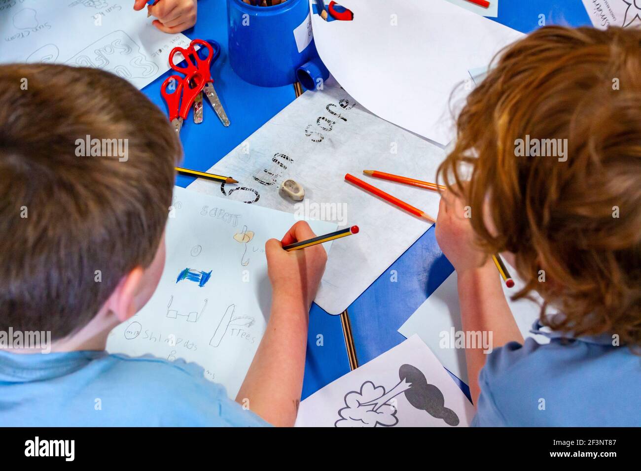 Grundschulkinder schreiben während einer Unterrichtsstunde auf einem Schreibtisch. Stockfoto