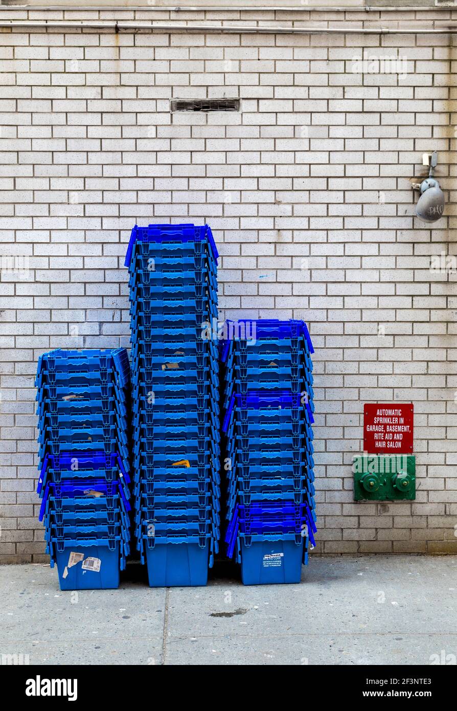 Gestapelte Container auf einem Bürgersteig mit einem Hydranten und Licht vor einer verglasten Wand. Stockfoto