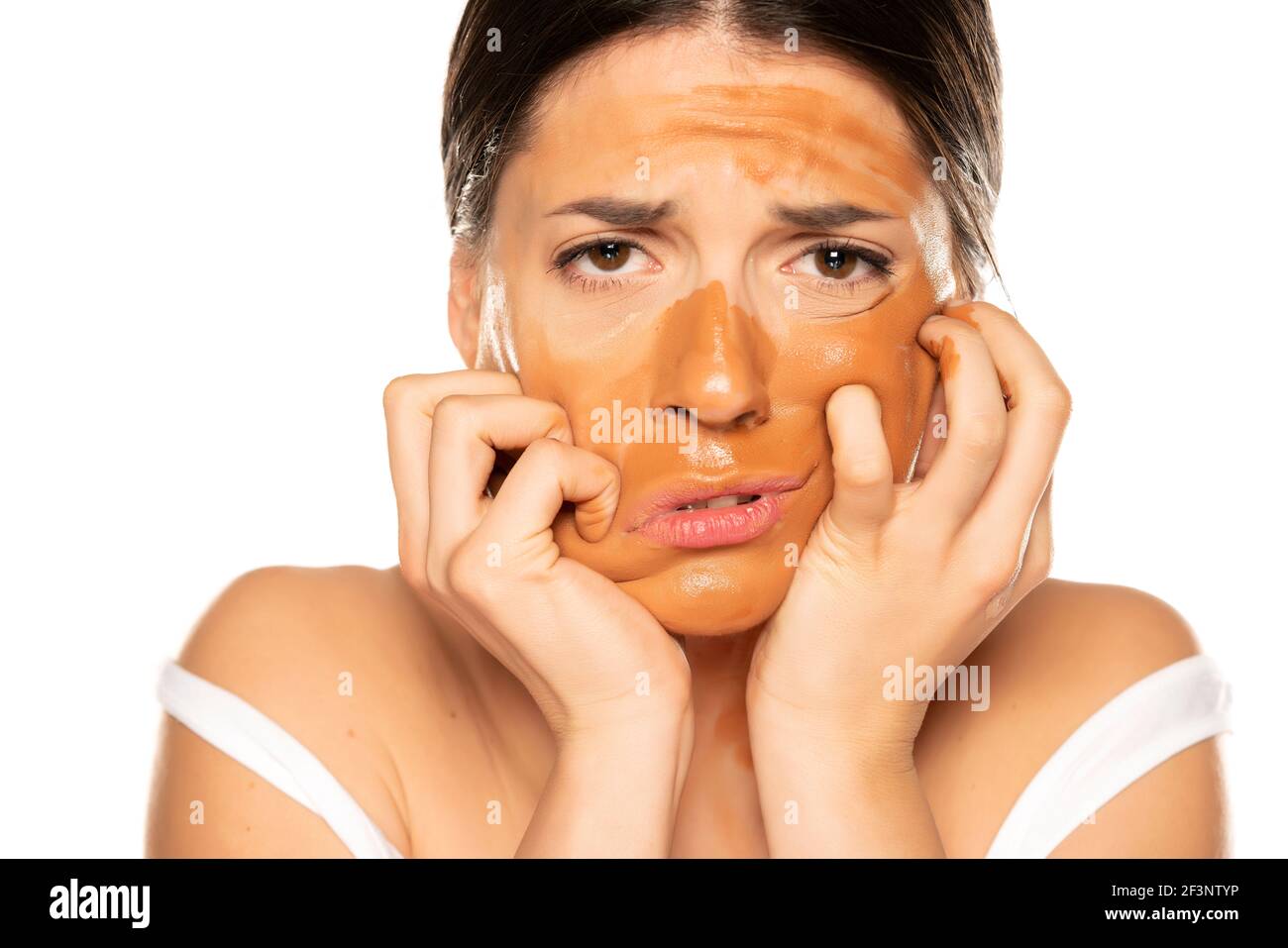 Junge enttäuschte Frau mit falschen Make-up-Basis auf ihrem Gesicht Auf weißem Hintergrund Stockfoto