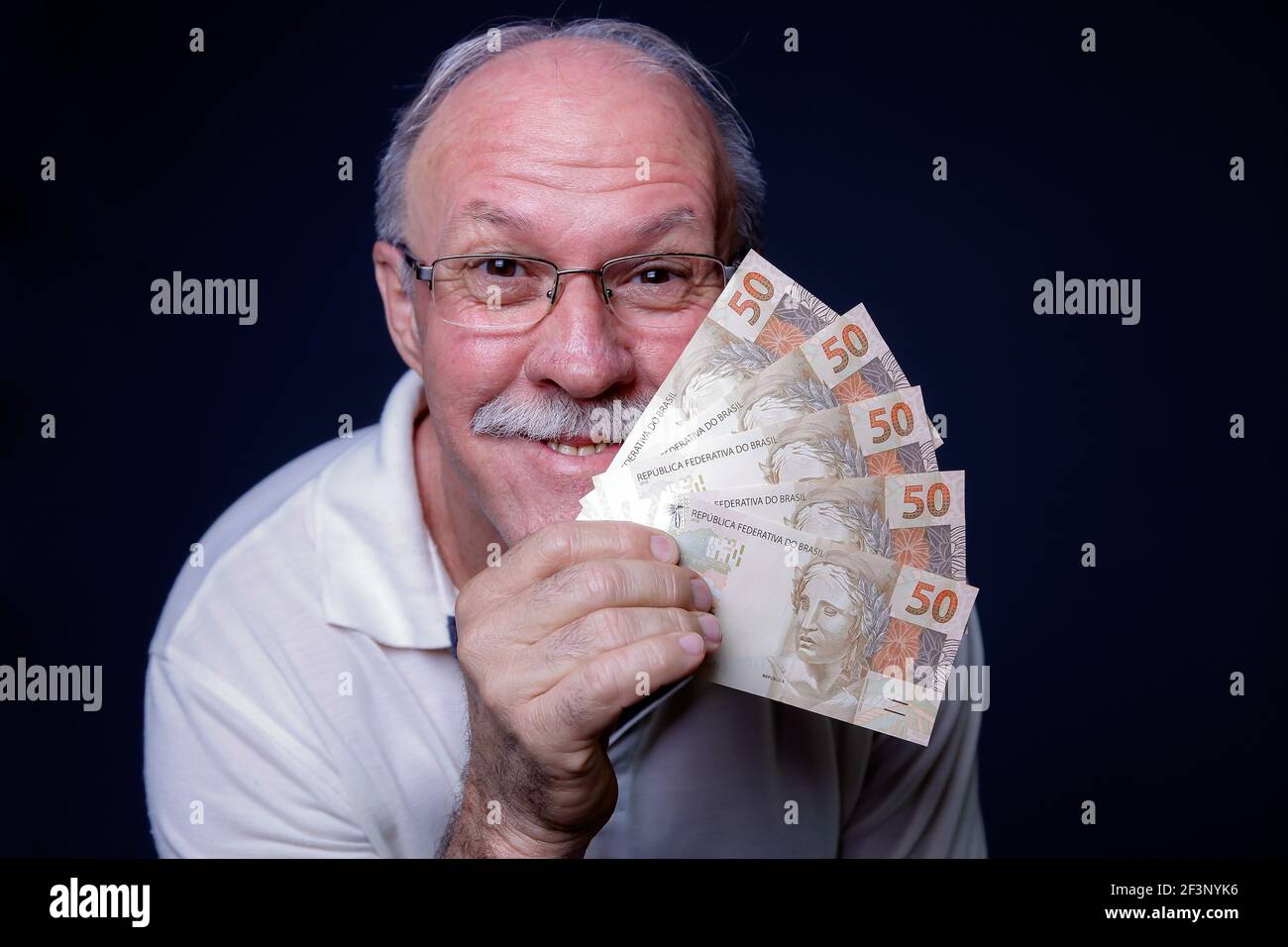 Weißer Erwachsener Mann lächelt an der Kamera und hält mehrere Brasilianer Echtgeldrechnungen Stockfoto