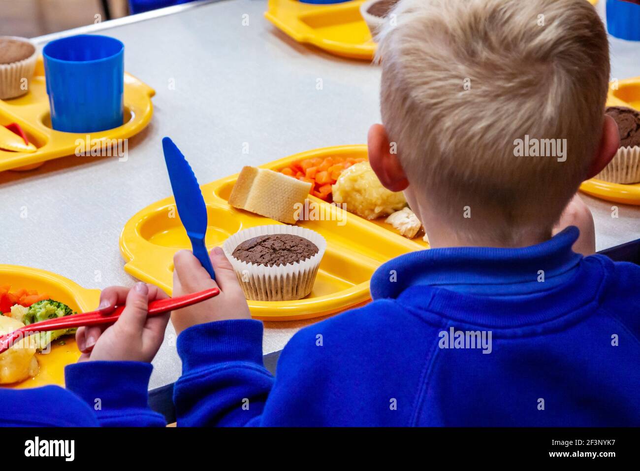 Kinder in einer Grundschule essen Schule Abendessen mit Plastiktellern, Tassen und Besteck. Stockfoto
