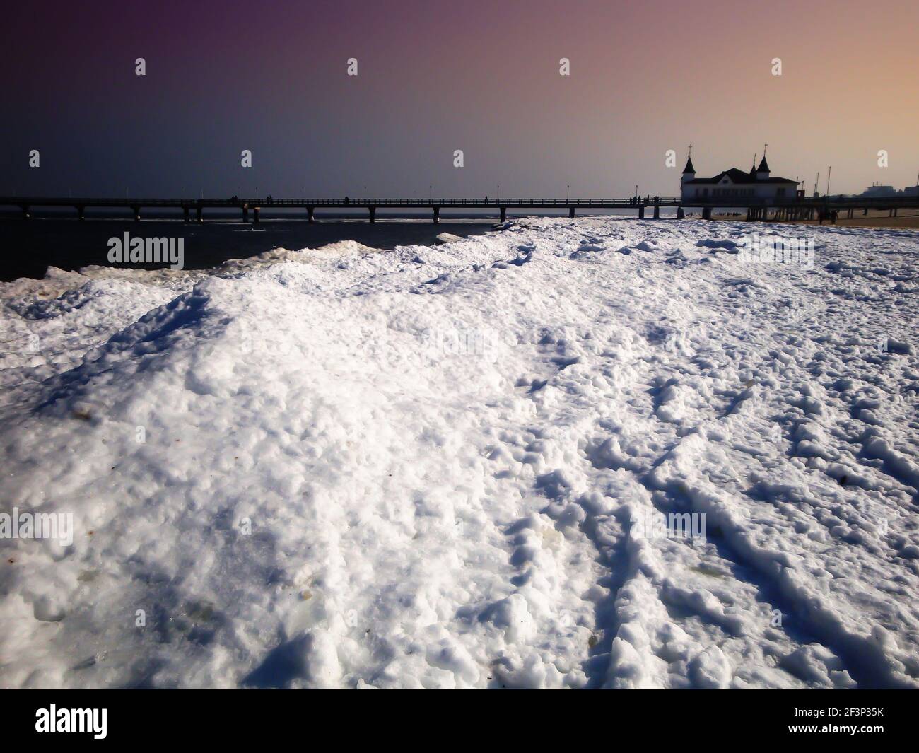 Usedom Strand mit Schnee, ein Pier im Hintergrund. Abendstimmung an einem kalten Wintertag, mit einem violetten Himmel. Stockfoto