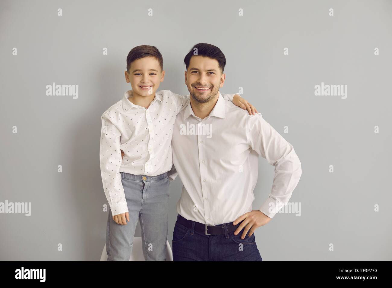 Porträt von Papa mit kleinen Sohn umarmt und Blick auf die Kamera auf grauem Hintergrund. Stockfoto