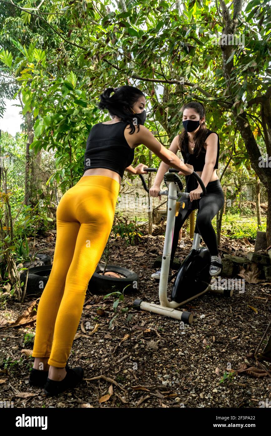 Zwei junge Frauen, die das Beste aus einem Statik herausholen Radfahren, um gemeinsam im Freien in einer rustikalen Umgebung zu trainieren Auf einem Hinterhof in Kuba Stockfoto