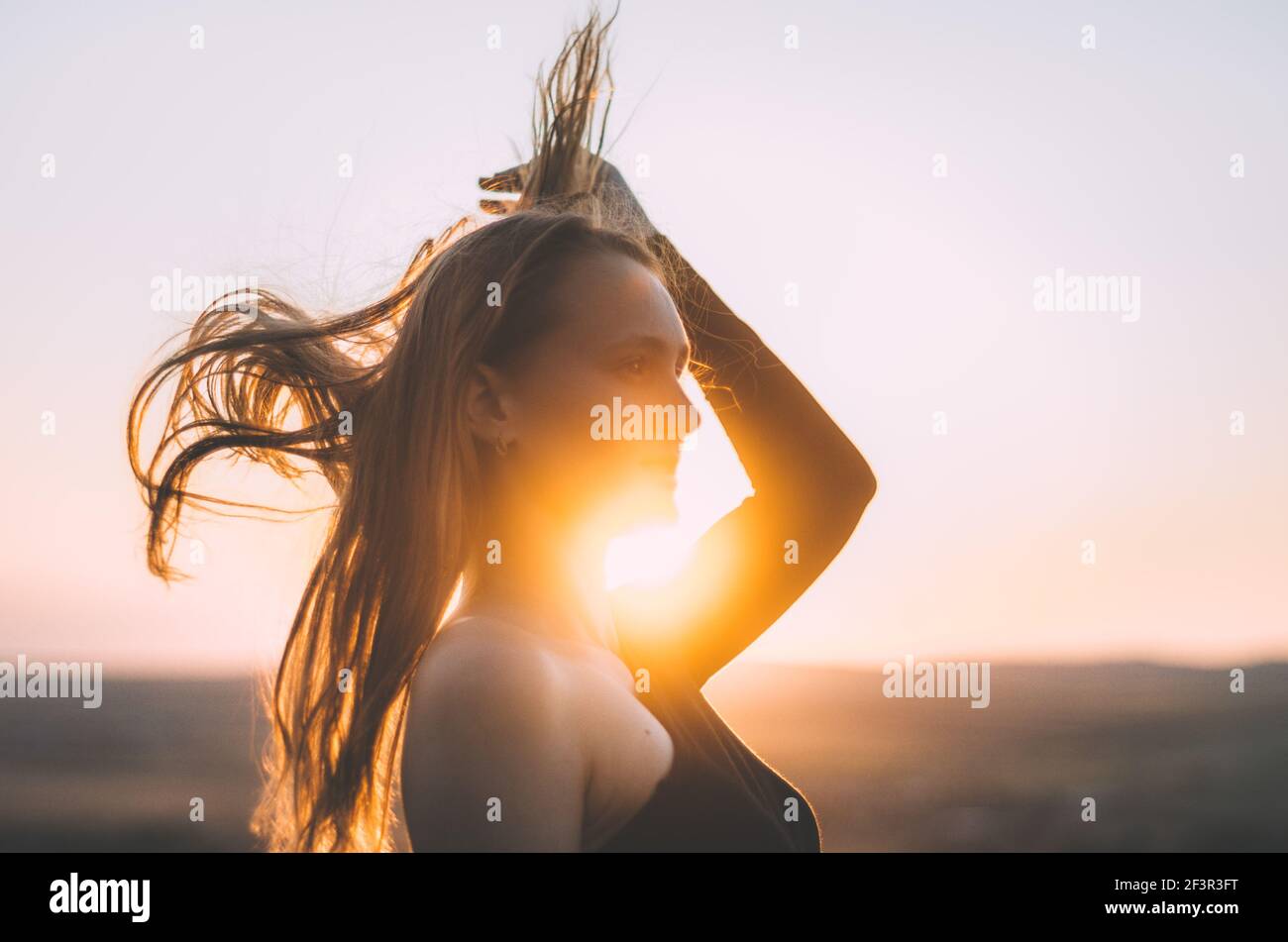 Künstlerische Oberkörper Seitenansicht Porträt einer jungen kaukasischen Frau Rahmen der Sonnenuntergang goldenes Licht mit gebogenen Ellbogen, tun Haare werfen Stockfoto