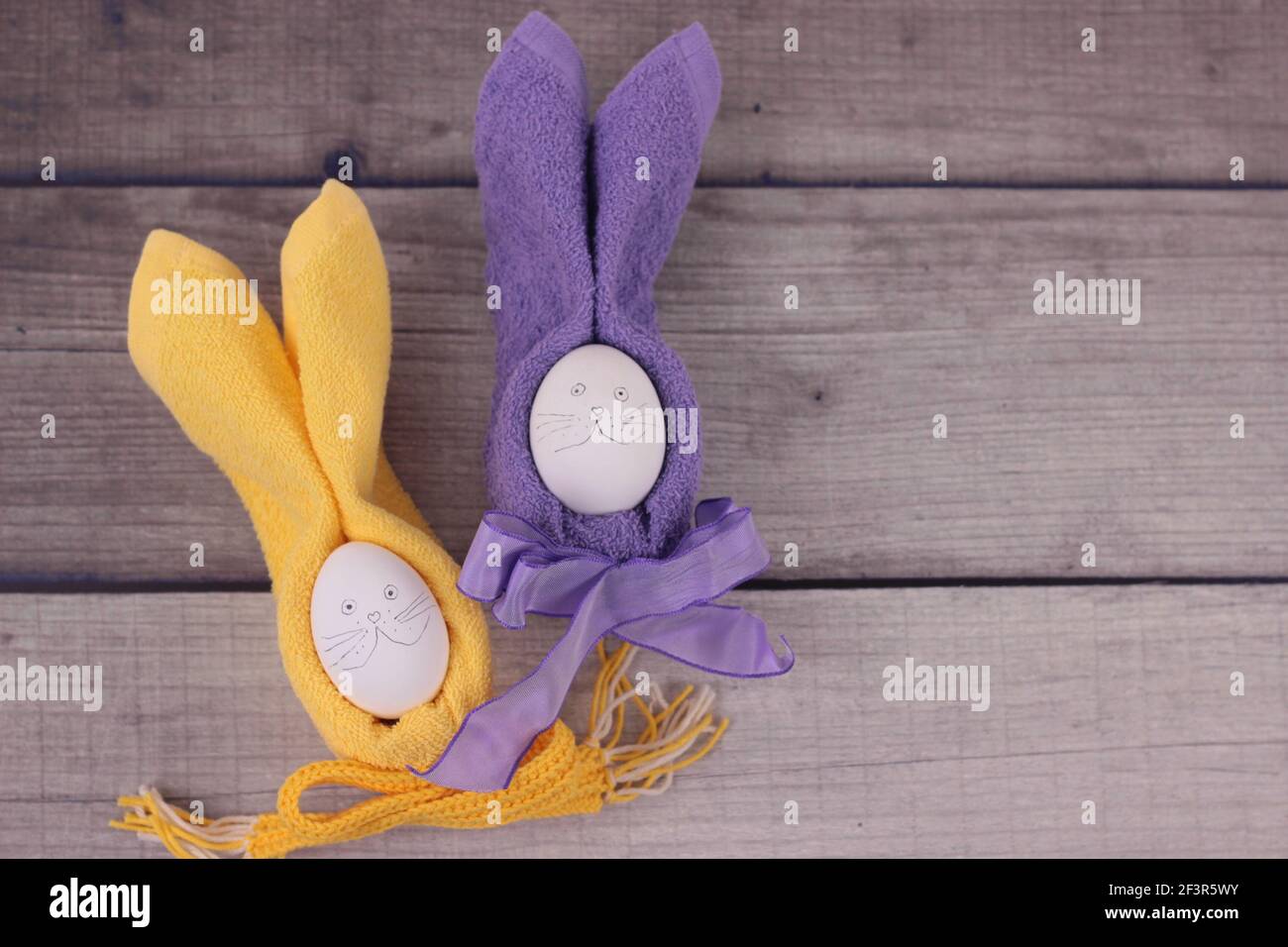 Frohe ostern Konzept.Ostern Feiertags Tisch Einstellung mit Eiern auf Scheune Boards. Rubbits aus Eiern, gelbe und violette Servietten mit Schleifen auf Holzhintergrun Stockfoto
