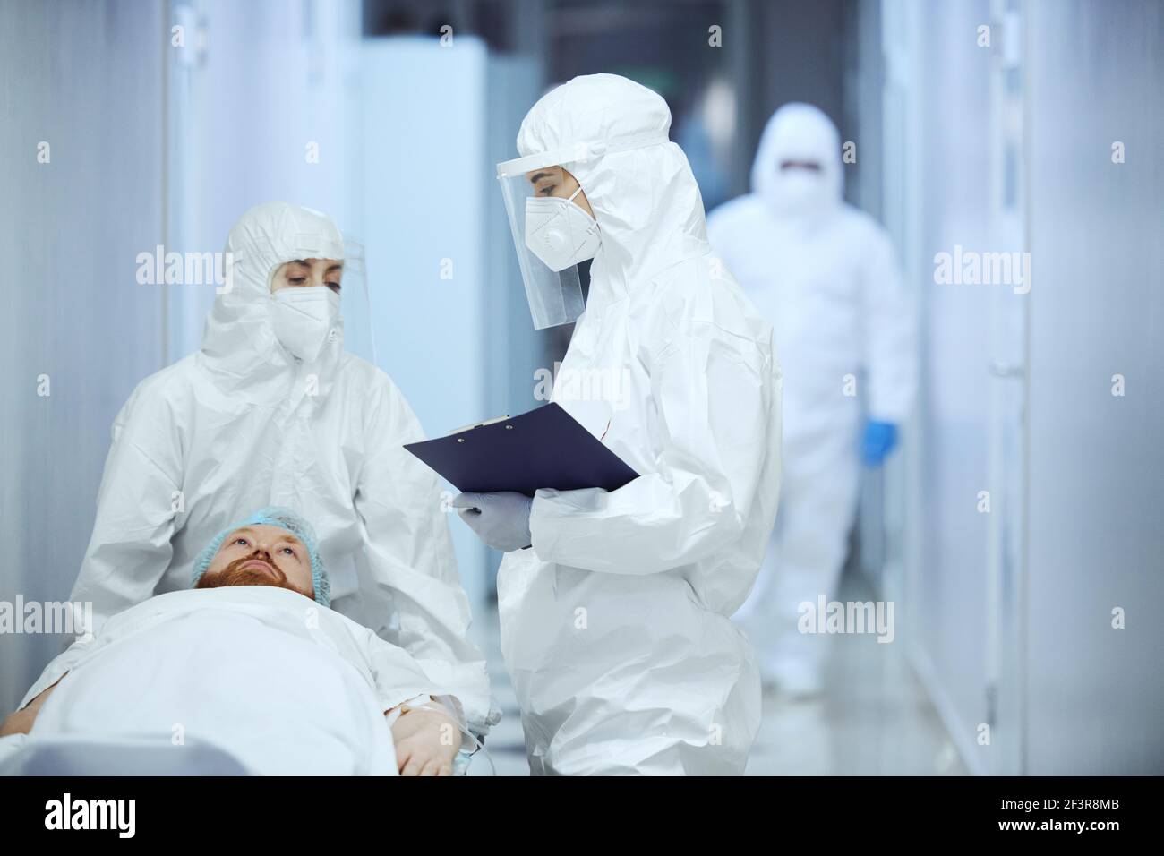 Verletzter Patient liegt auf einer Liege, mit zwei Ärzten im Gespräch Einander im Krankenhaus Stockfoto