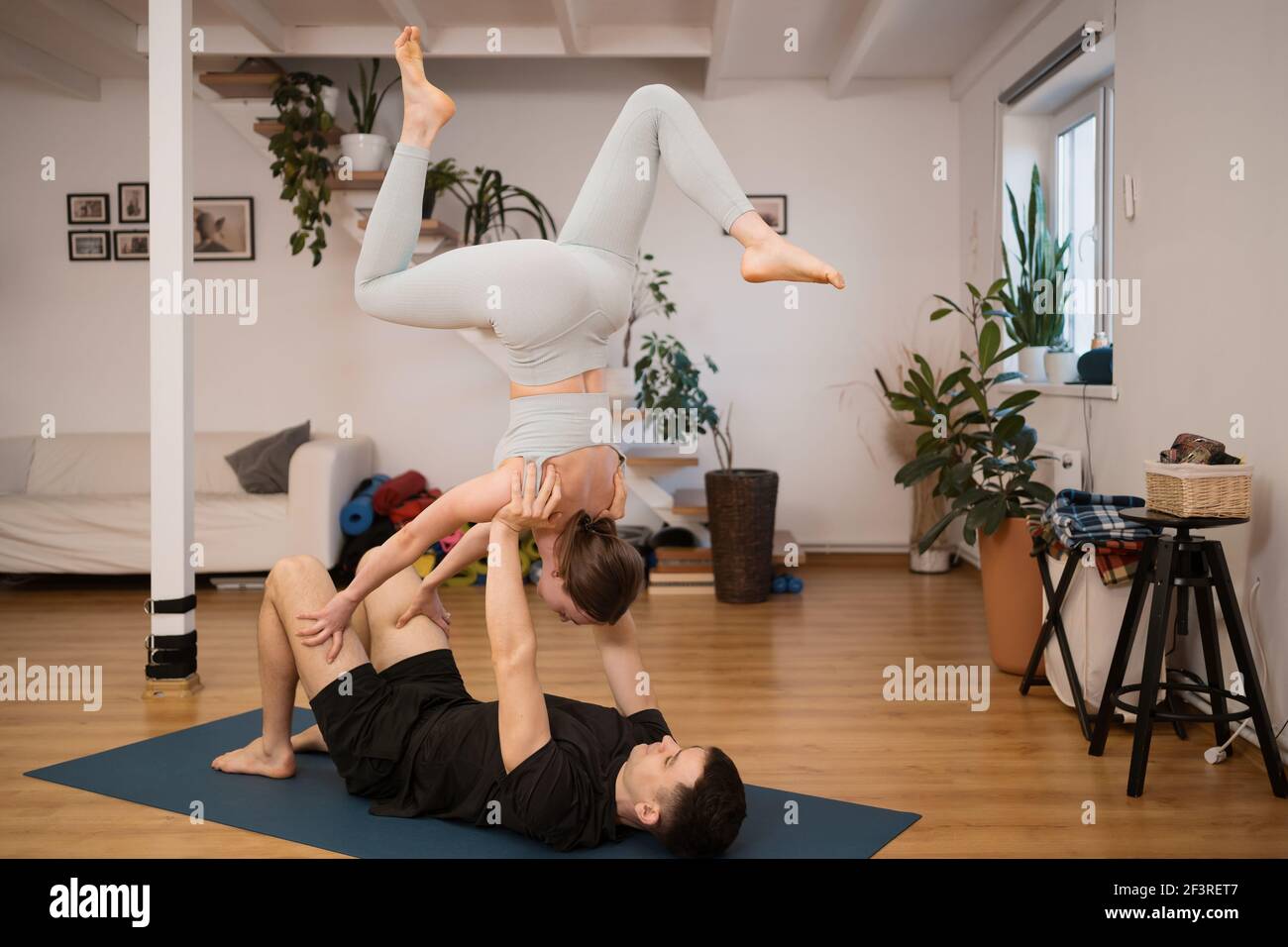 Junges Paar, das gemeinsam Yoga praktiziert, zu Hause in einem modernen Interieur. Hobby, Zweisamkeit, gesunder Lebensstil Stockfoto