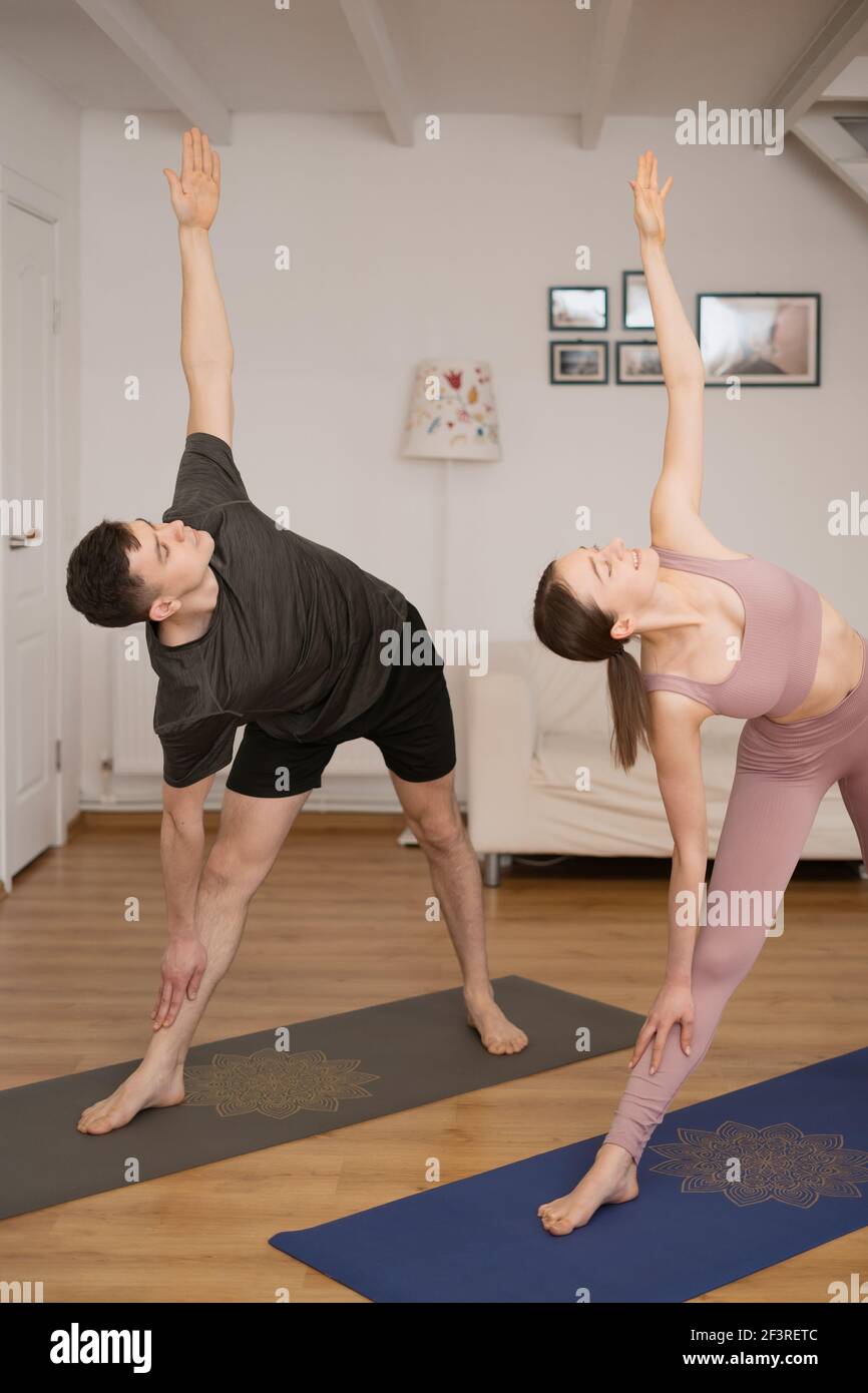Junges Paar, das gemeinsam Yoga praktiziert, zu Hause in einem modernen Interieur. Hobby, Zweisamkeit, gesunder Lebensstil Stockfoto