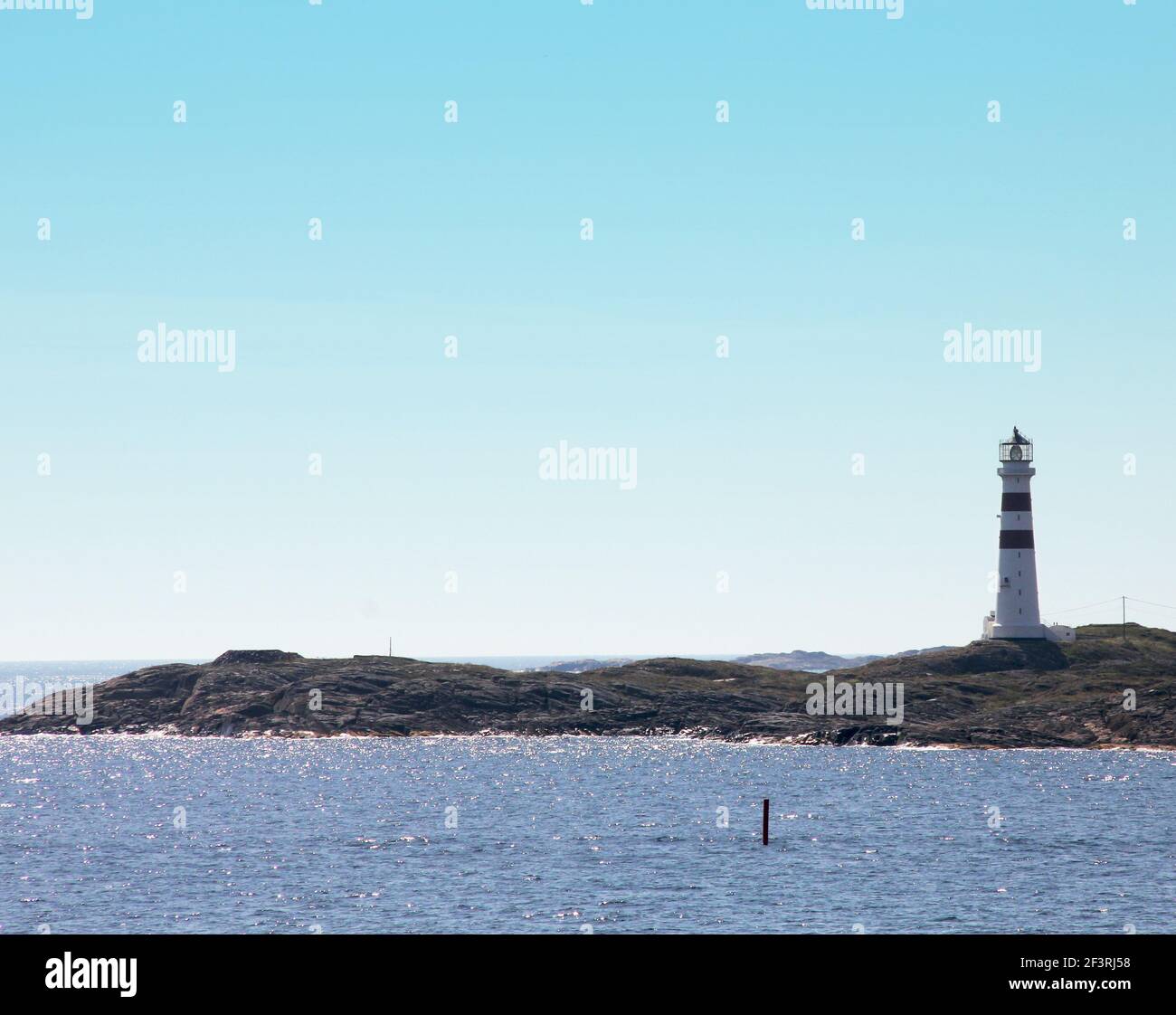 Eine Meereslandschaft mit einer kleinen Insel mit einem Leuchtturm darauf. Der Leuchtturm ist weiß mit roten Streifen. Stockfoto