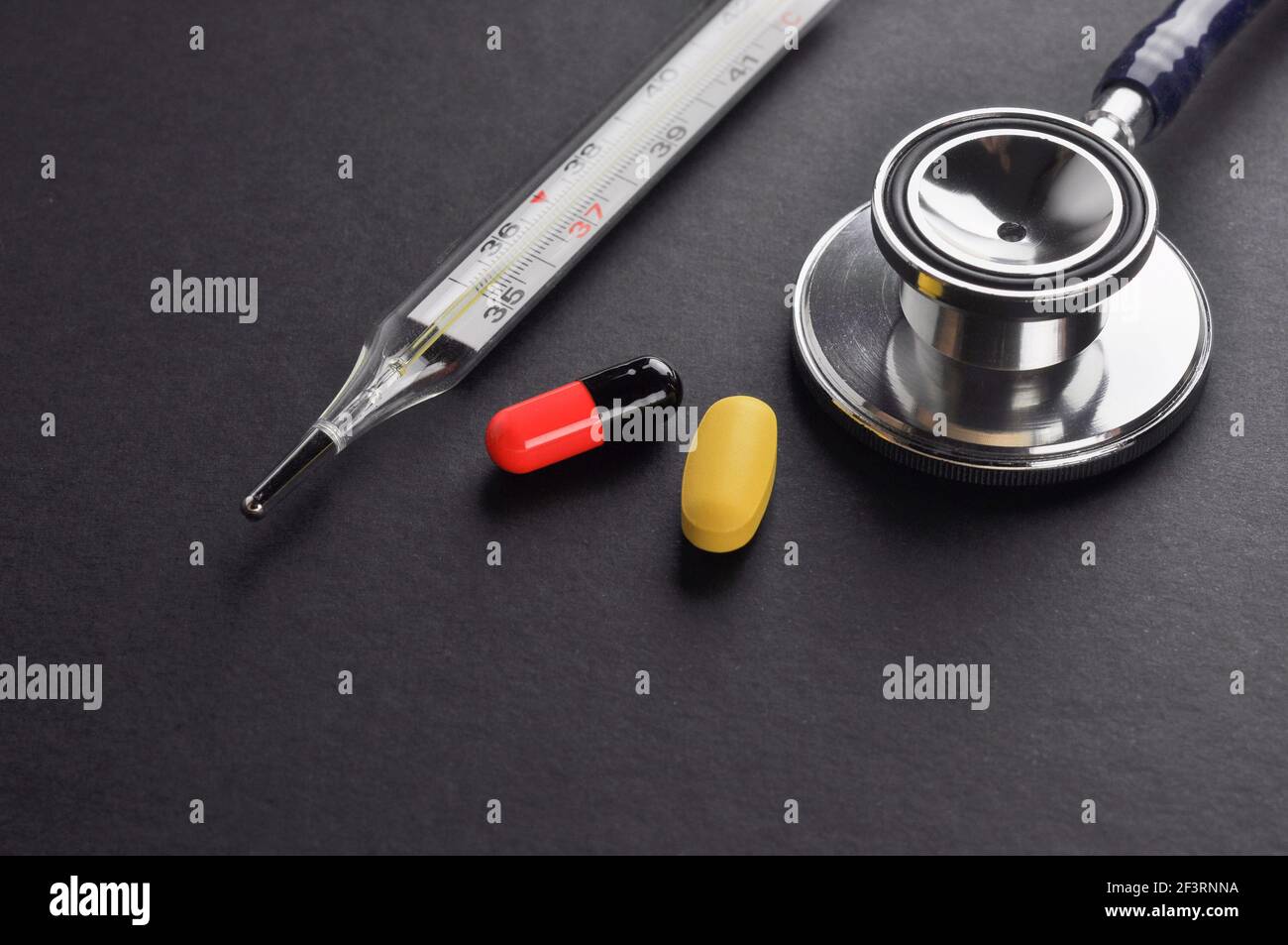 Stethoskop, Thermometer, Pillen und Kapsel auf schwarzer Oberfläche. Diagnose- und Behandlungskonzept. Stockfoto