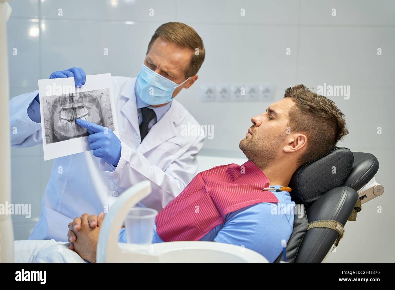 Besorgter Zahnchirurg, der ein Röntgenbild in der Nähe seines Patienten hält Stockfoto
