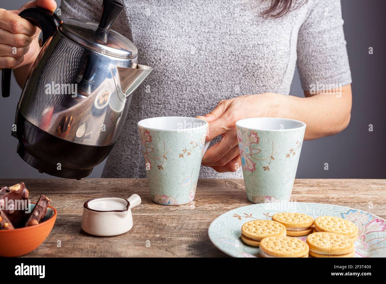 Ein Tee-Zeit- oder Kaffee-Zeit-Konzept mit Sandwich-Cookies, Tafeln aus schokoladenästhetischem Keramik-Becher und -Tellern sowie einem Mini-Creamer-Krug auf Holz Stockfoto