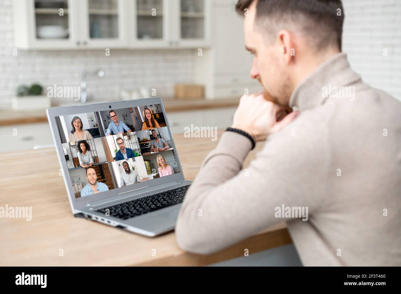 Ein männlicher Mitarbeiter hat eine Videokonferenz mit Kollegen, Rückansicht über die Schulter auf dem Laptop-Bildschirm mit einem vielfältigen Team darauf, Video-Meeting-Konzept Stockfoto