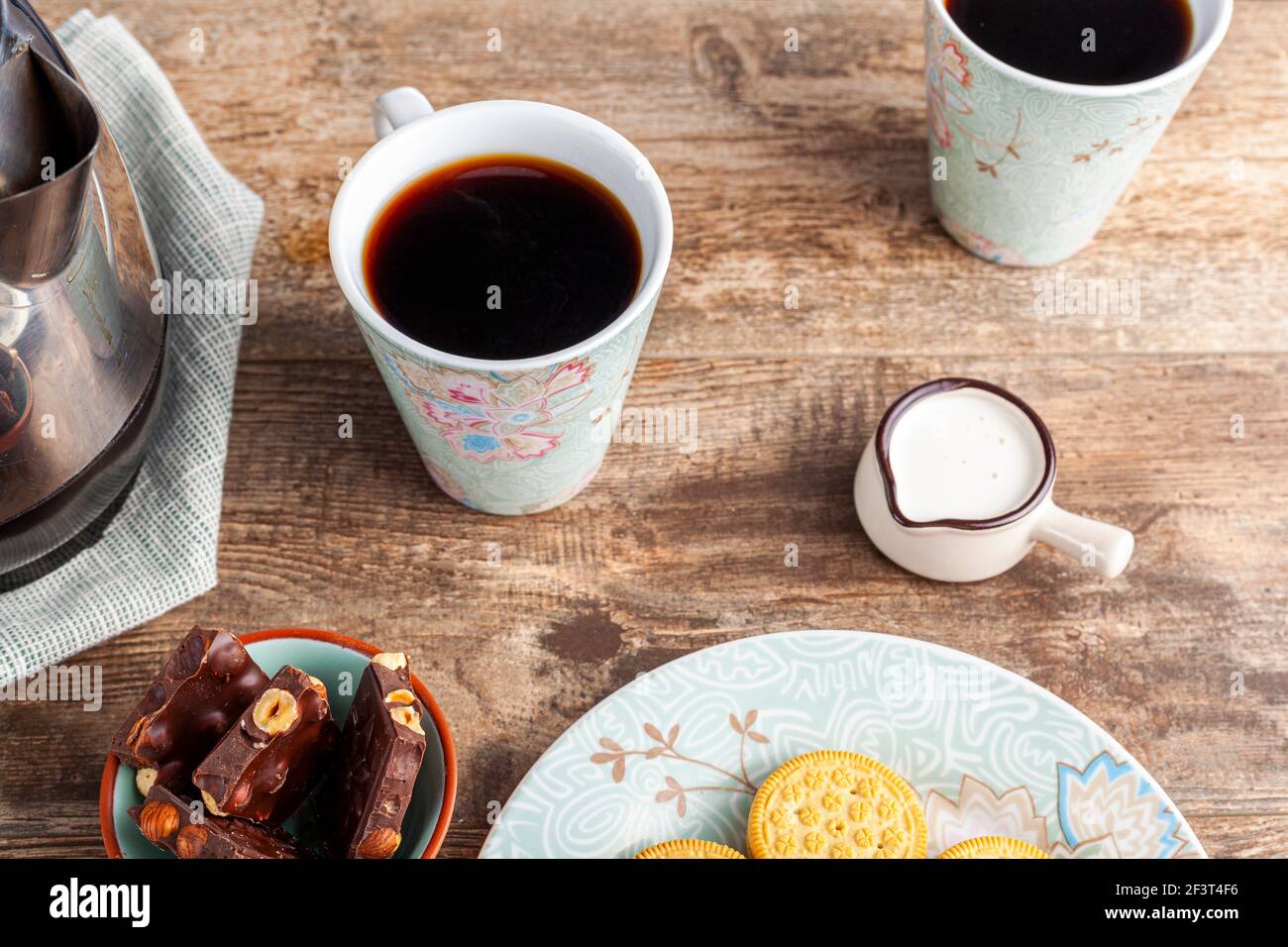 Ein Tee-Zeit- oder Kaffee-Zeit-Konzept mit Sandwich-Cookies, Tafeln aus schokoladenästhetischem Keramik-Becher und -Tellern sowie einem Mini-Creamer-Krug auf Holz Stockfoto