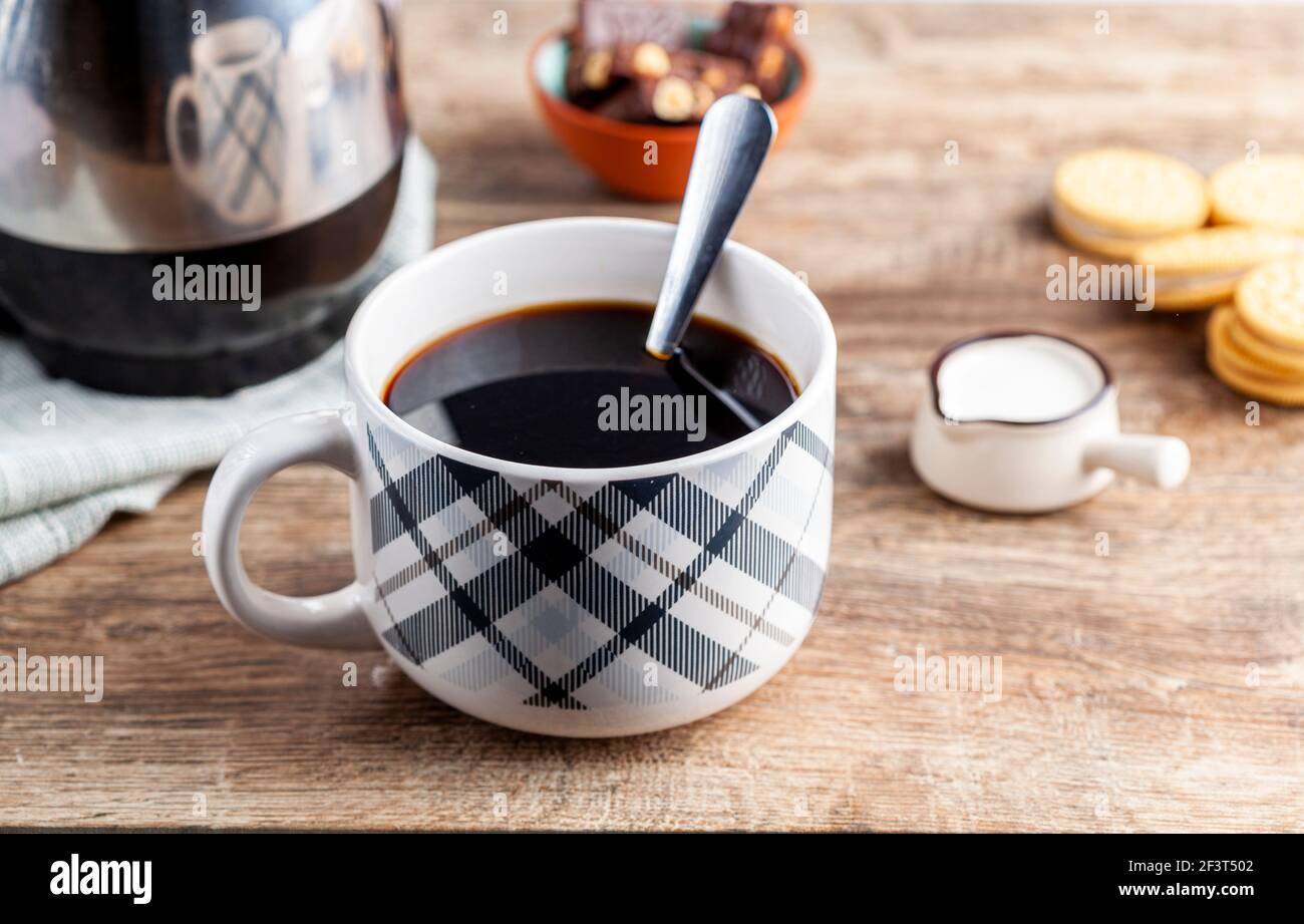 Ein Tee-Zeit- oder Kaffee-Zeit-Konzept mit Sandwich-Cookies, Tafeln aus schokoladenästhetischem Keramik-Becher und -Tellern sowie einem Mini-Creamer-Krug auf Holz Stockfoto