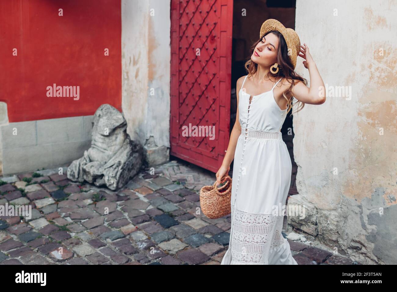 Outdoor-Porträt der jungen Frau trägt stilvolle weiße Sommerkleid und Accessoires in alten Lviv Stadt. Modischer Strohhut und Geldbörse. Rock-Kleid Stockfoto