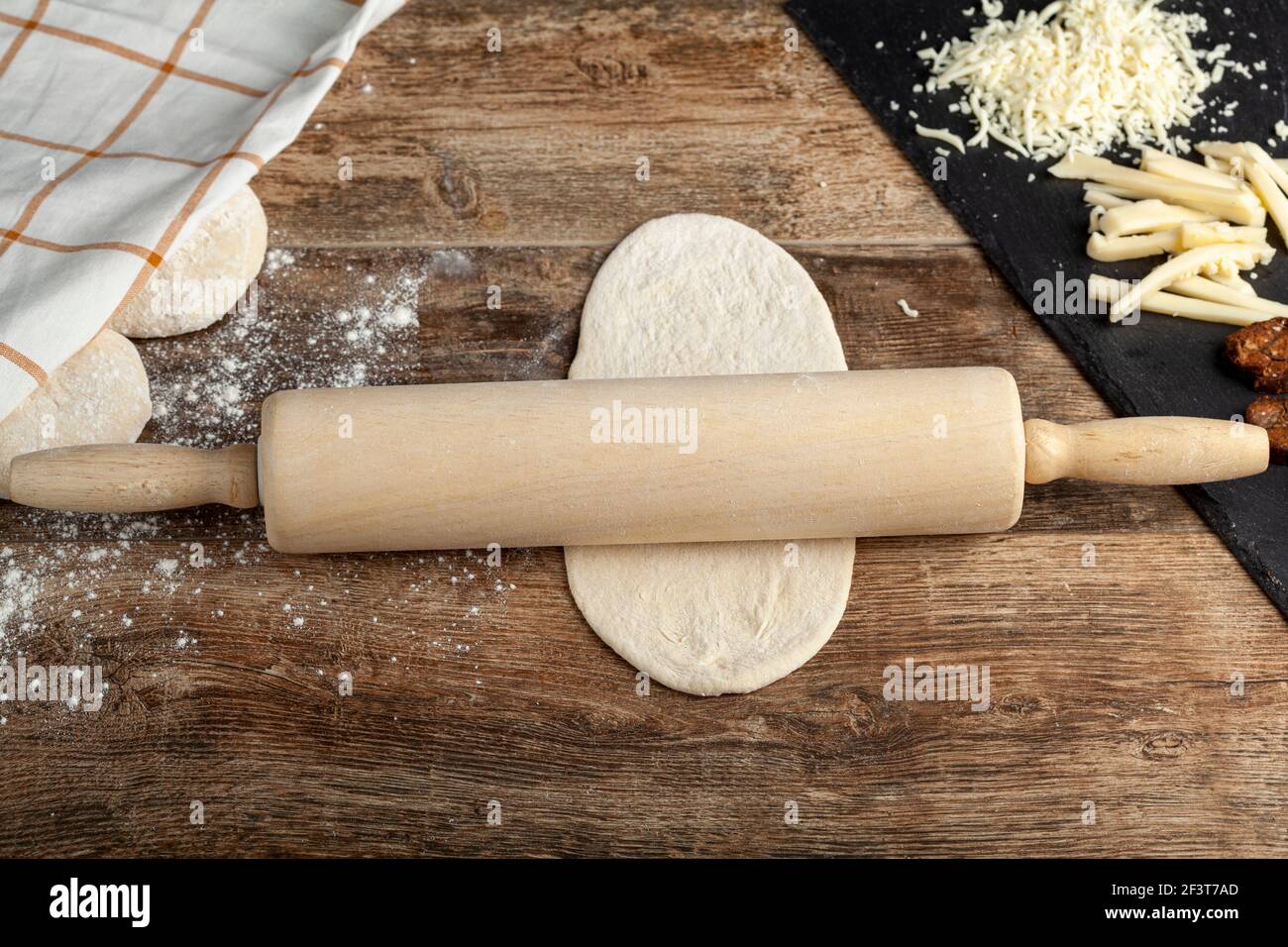 Nahaufnahme EIN Holzpfeifholz auf einem abgeflachten Teig auf einer Küchenarbeitsplatten aus Holz. Ein Konzept für die Brotherstellung mit Lafs und Käse und Su Stockfoto