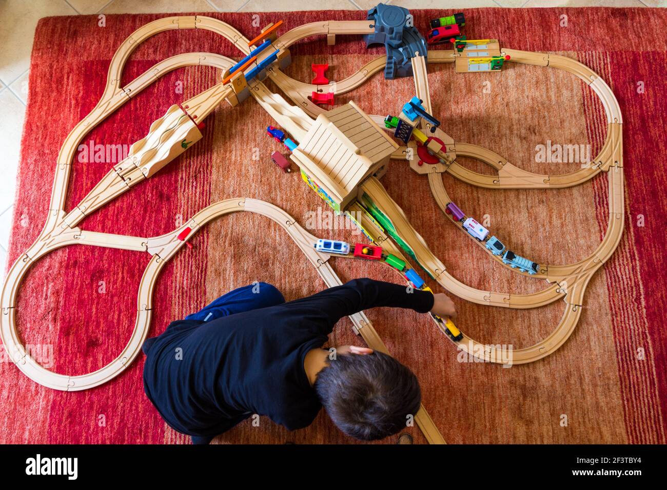Draufsicht auf das Kind, das mit einer hölzernen Eisenbahnstrecke spielt Teppich zu Hause Stockfoto
