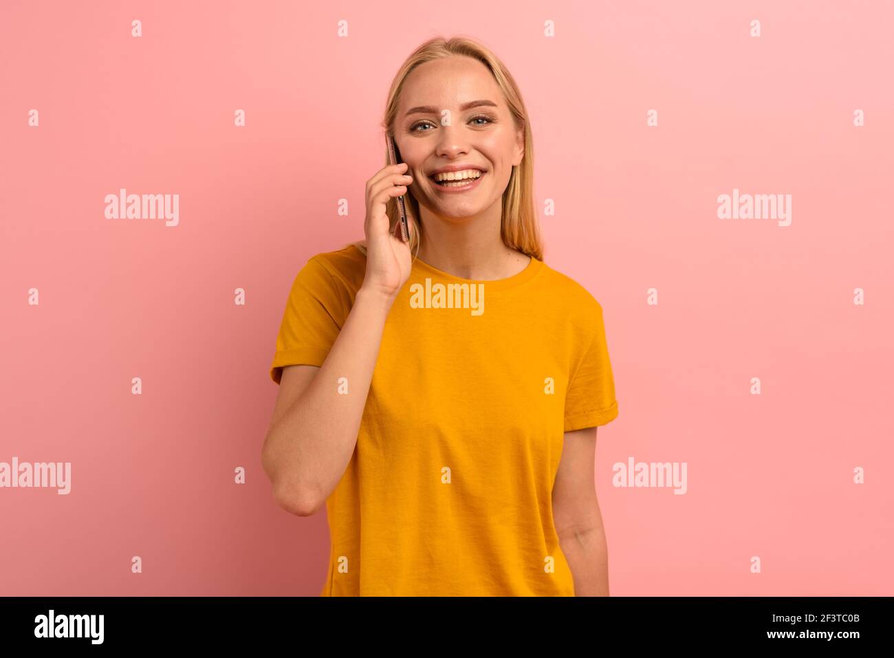 Blonde Frau spricht am Telefon mit Freunden. Fröhlicher Ausdruck. Rosa Hintergrund Stockfoto