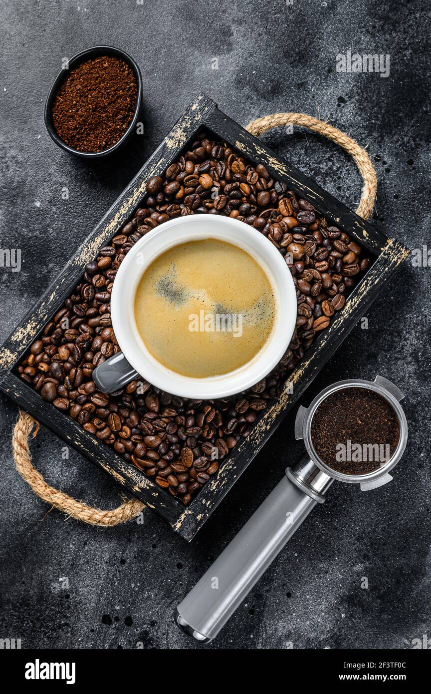 Kaffeetasse und Bohnen in alten Holztablett. Schwarzer Hintergrund. Draufsicht Stockfoto